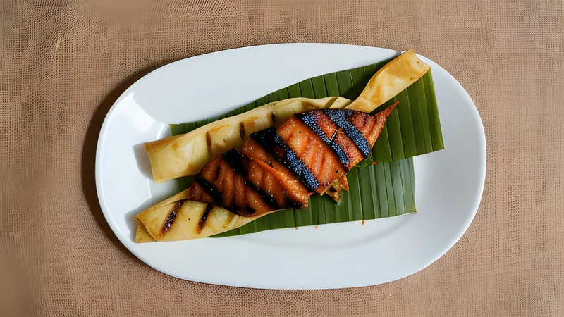 Grilled otak-otak fish parcels in banana leaf, charred and unwrapped on a plate