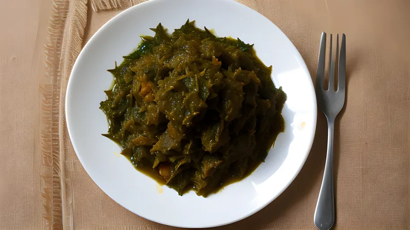 Deep green saka saka cassava leaf stew simmering in a dark pot with a slick of red palm oil